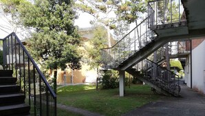 A courtyard with a staircase leading to an upper level, surrounded by trees and a building.