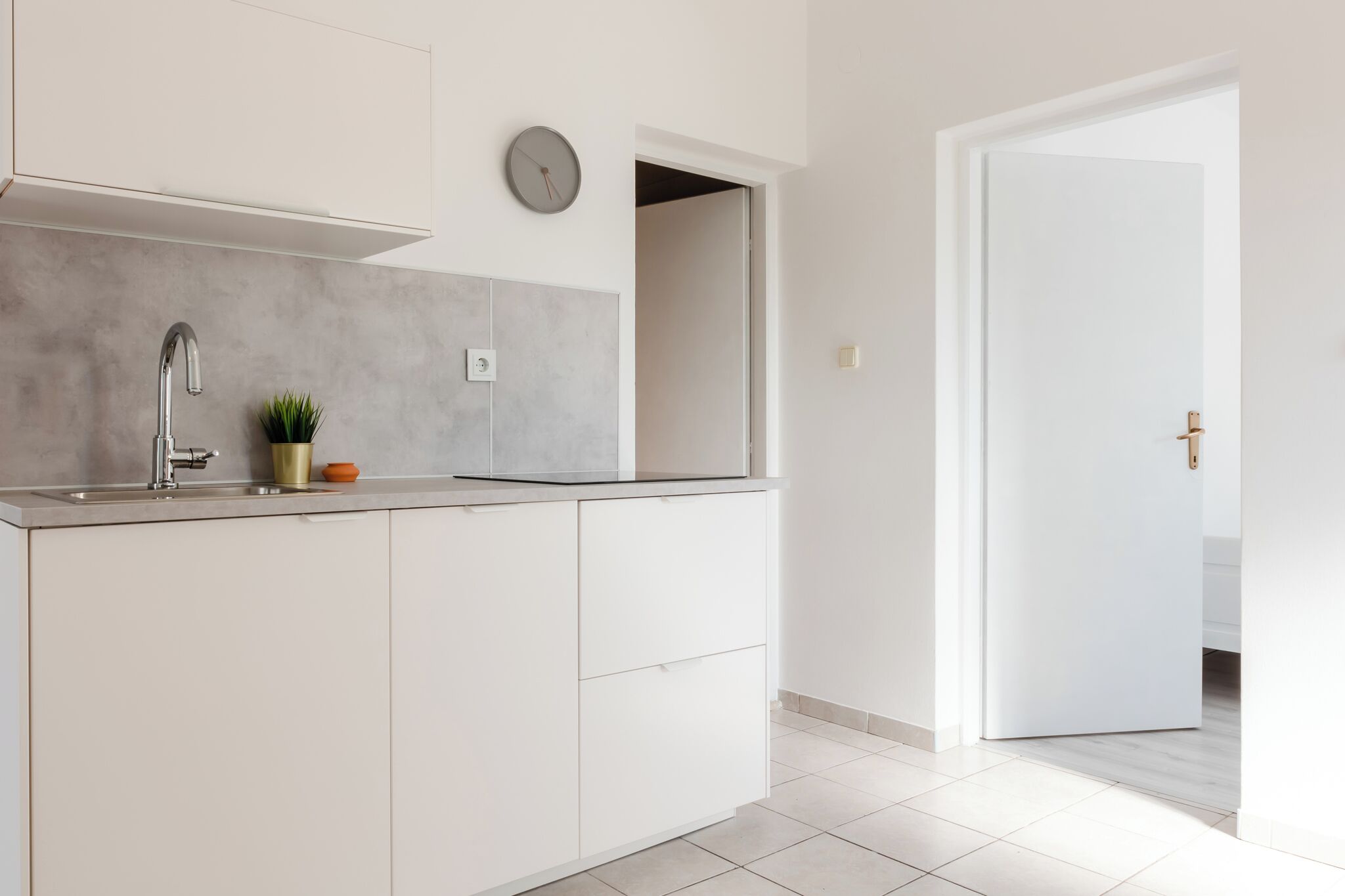 Une cuisine moderne dotée d’un évier encastré, d’une horloge au mur et d’une porte donnant sur une autre pièce.