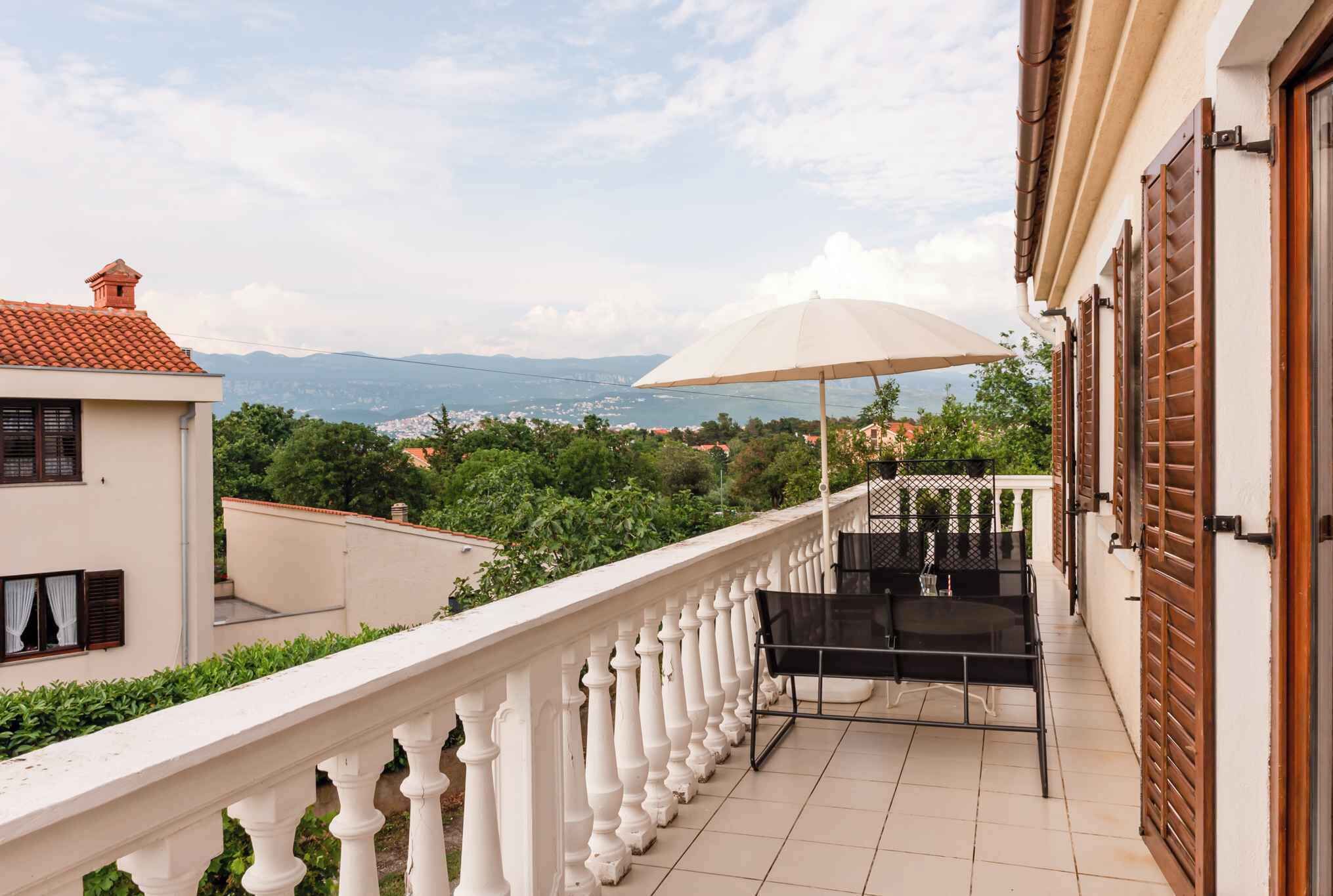 A balcony with a white balustrade, a table with chairs, and a large umbrella.