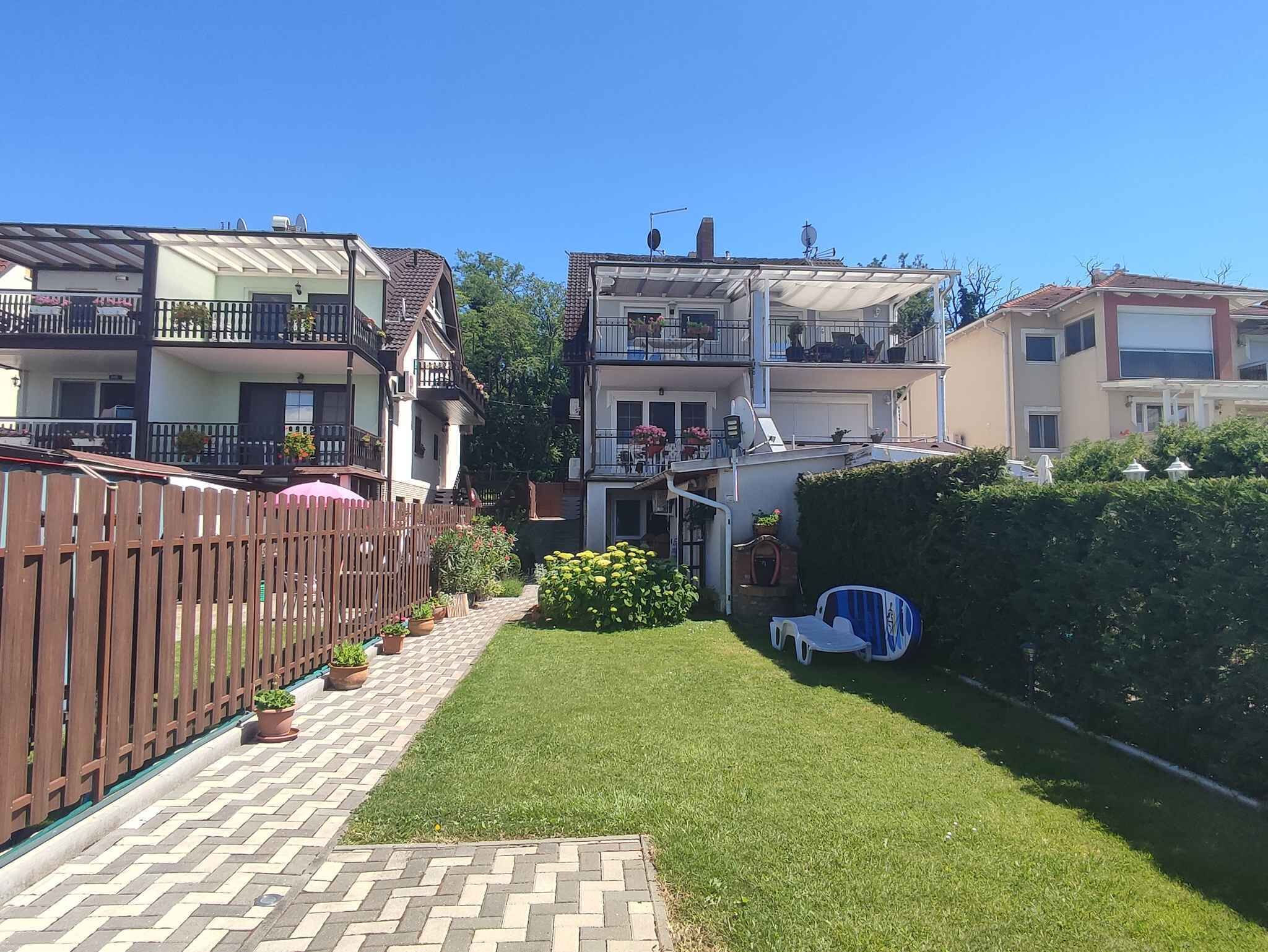A residential area with a well-maintained lawn, a wooden fence, and a pathway leading to a house with a balcony.