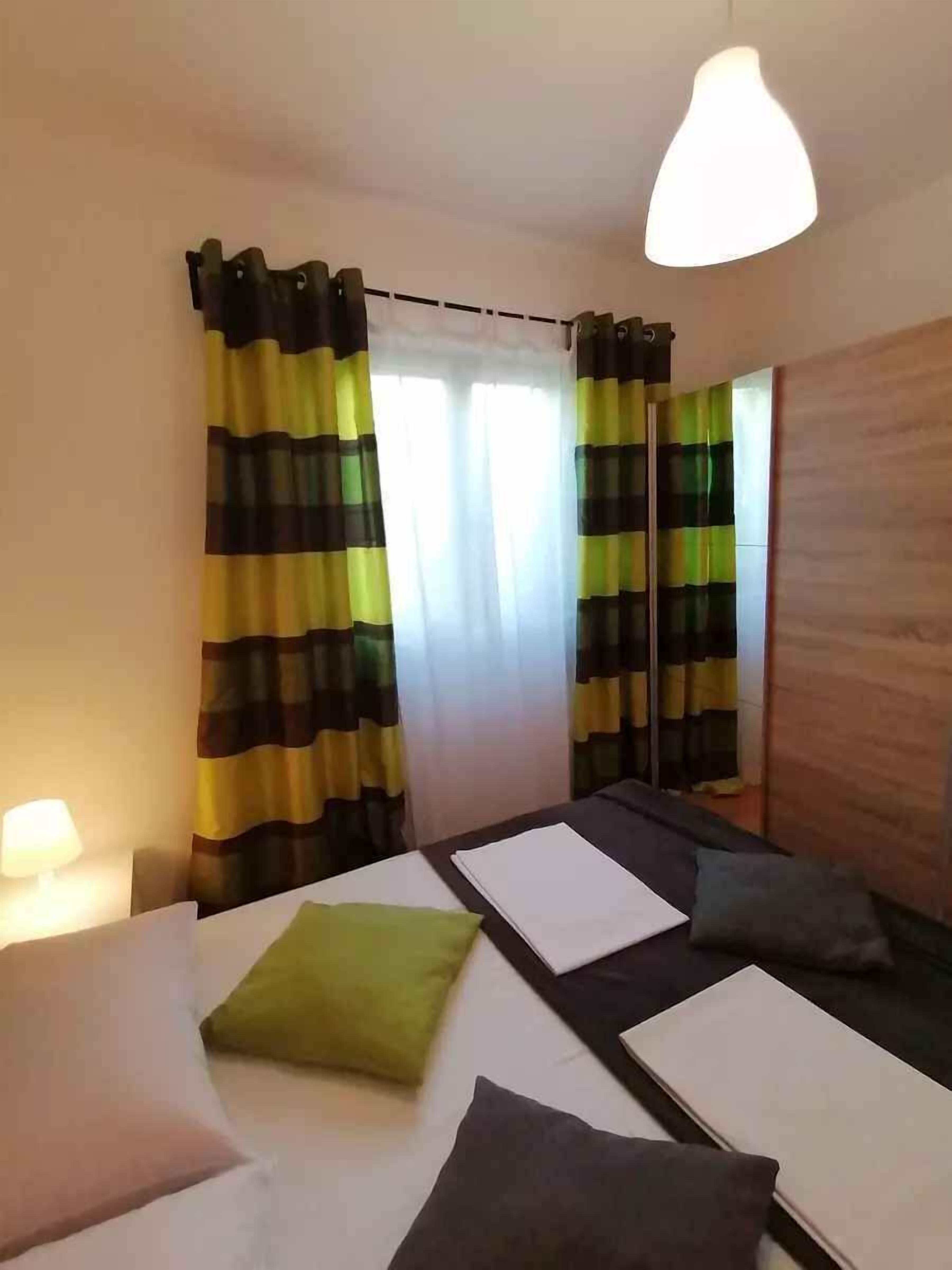 A room with two beds, a wooden wardrobe, and a window with striped curtains.