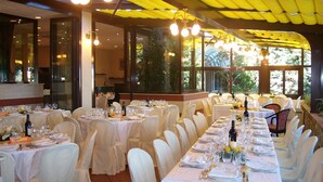 A banquet hall with multiple round tables set for dining, large windows, and hanging light fixtures. - Studio mit Pool (Imperia)