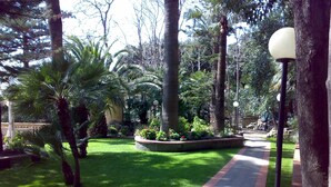 A pathway through a well-maintained garden with various trees and a lamp post. - Studio mit Pool (Imperia)
