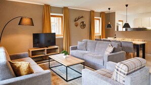 Ein modernes Wohnzimmer mit Flachbildfernseher, grauen Sofas, einem Holztisch und einem Essbereich mit Tisch und Stühlen.