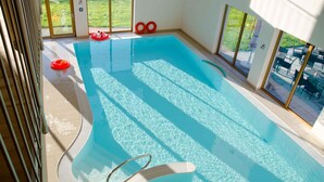 Ein Hallenbad mit klarem Wasser, einem Sprungbrett und Blick ins Freie durch große Fenster.
