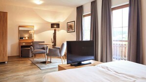 Ein Hotelzimmer mit einem Bett, einem Schreibtisch mit Stuhl, einem Fernseher und einem großen Fenster mit Vorhängen.