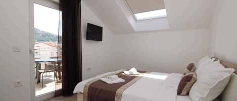 A bedroom with a bed, a TV, a skylight, and a view of the outside.