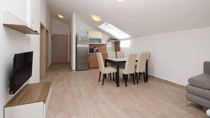 A modern apartment with a dining area, kitchenette, and a TV mounted on the wall. - Holiday apartment with air conditioning and Wi-Fi (Baška)