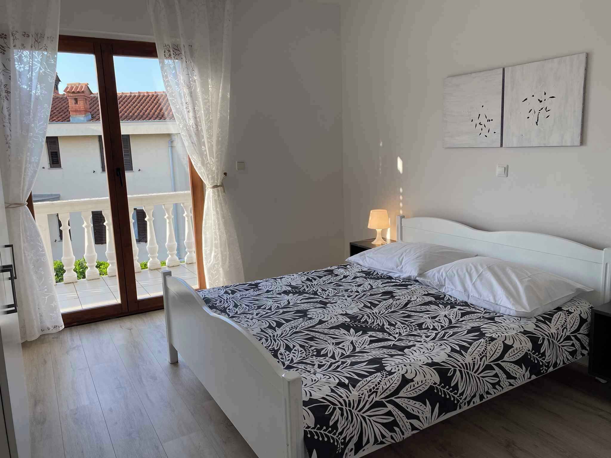 Un dormitorio con cama, mesita de noche, lámpara y vistas a un balcón.