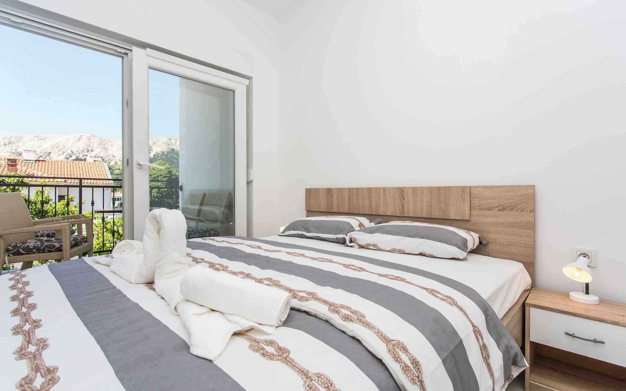 Quarto com cama, mesa de cabeceira, luminária, cadeira e varanda com vista para as montanhas.