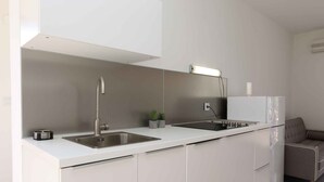 A modern kitchen with white cabinetry, stainless steel sinks, and a built-in oven.
