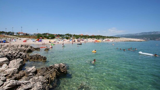 A beach with clear water, rocky shore, and people swimming and sunbathing.