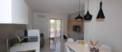 A modern kitchen with a built-in oven, a sink, and a dining area with a white table and chairs.