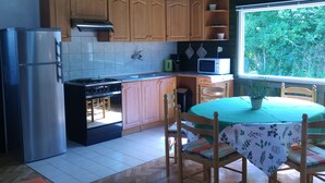 A compact kitchen with wooden cabinets, a stainless steel refrigerator, a stove, and a microwave. There's a dining table with chairs and a window with a view of greenery outside. - Holiday home with washing machine and smart TV (Valbandon)