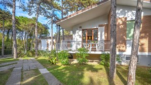 Een modern huis met twee verdiepingen en een overdekte veranda, omringd door bomen en een stenen pad.