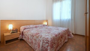 Een hotelkamer met een bed, nachtkastje, lamp en raam met gordijnen.