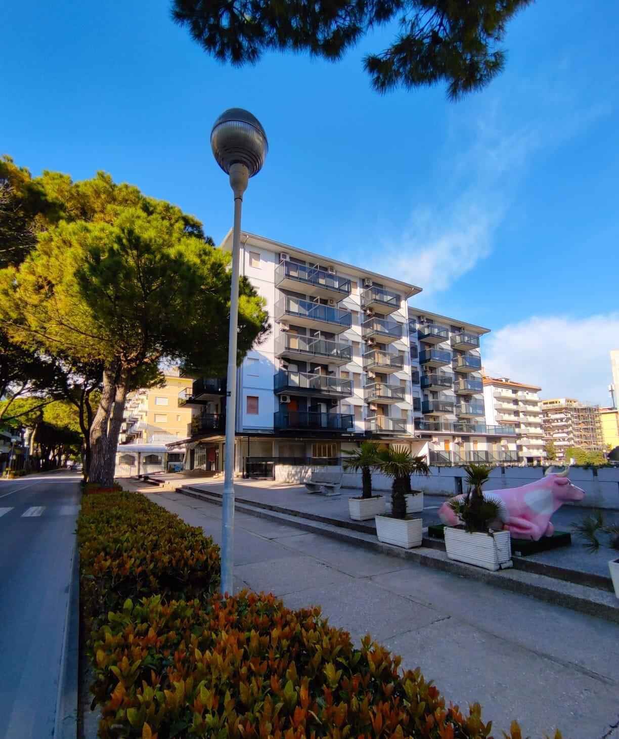 A modern multi-story building with balconies, a street lamp, and a decorative pink bull statue.