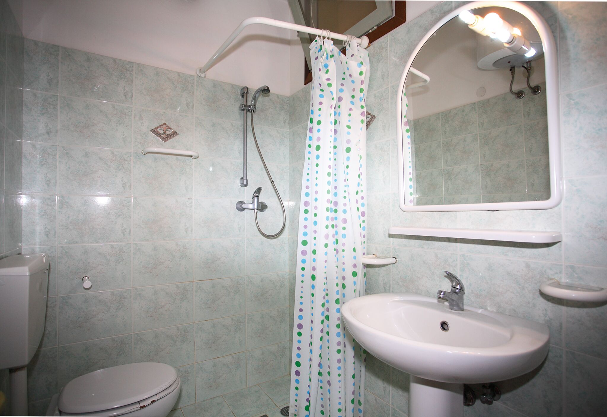 A bathroom with a toilet, sink, shower, and a mirror.