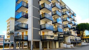 Ein mehrstöckiges Gebäude mit Balkonen und einer glatten Fassade, blauer Himmel.