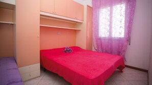 Ein Schlafzimmer mit einem Einzelbett, einem Kleiderschrank und einem Fenster mit einem blumigen Vorhang.