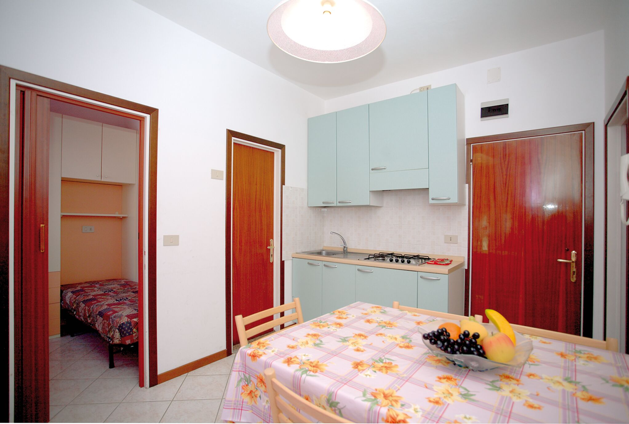 Una camera compatta con un letto, un tavolo da pranzo con una ciotola di frutta, angolo cottura e bagno.