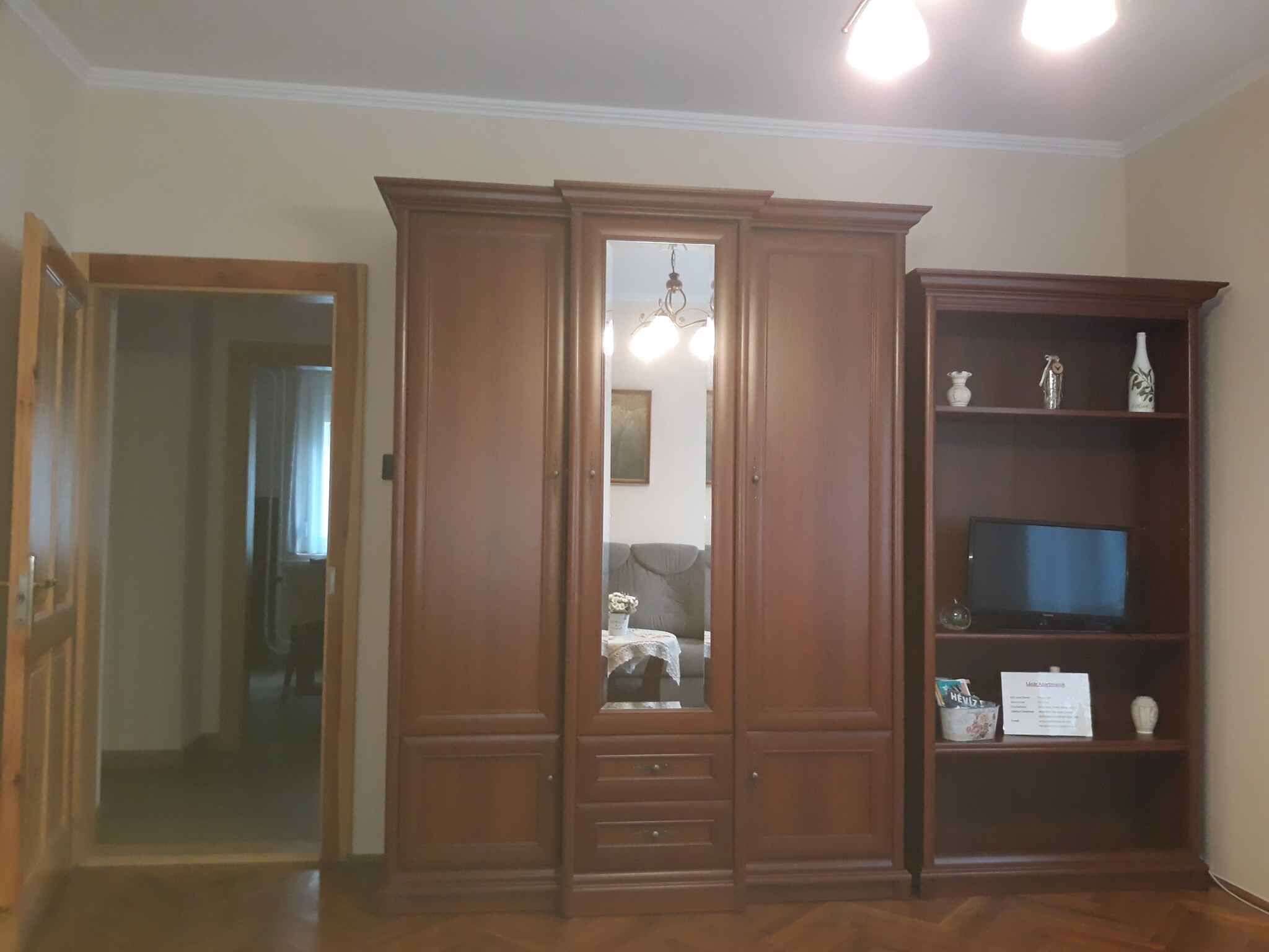 Une pièce avec une armoire en bois, un téléviseur posé sur une étagère et un miroir.
