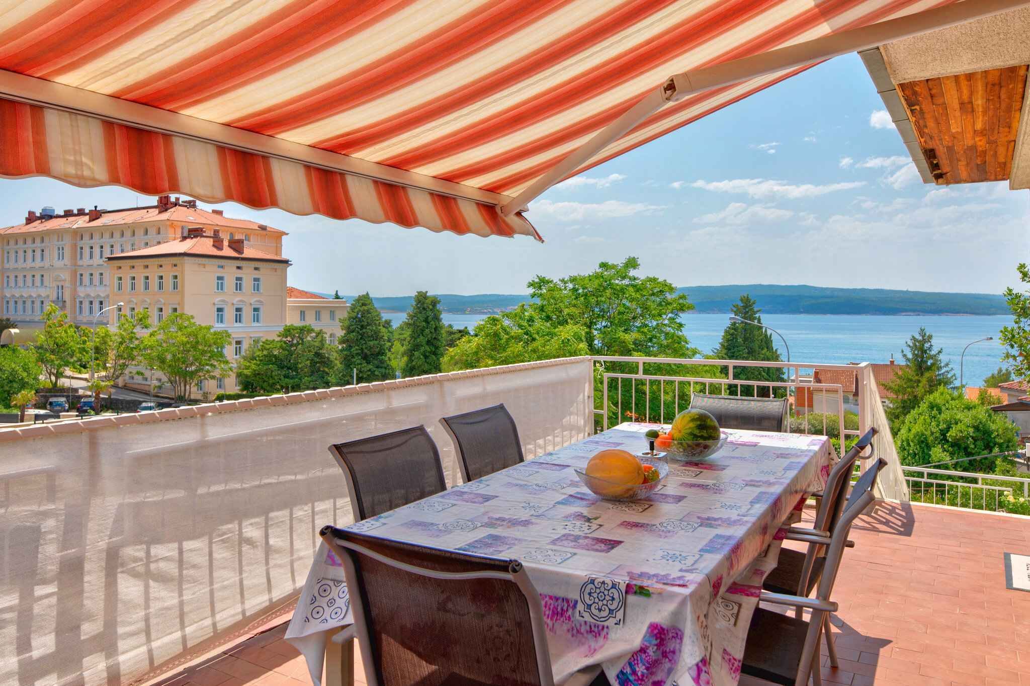 An outdoor dining area with a table set for two, overlooking a body of water and buildings.