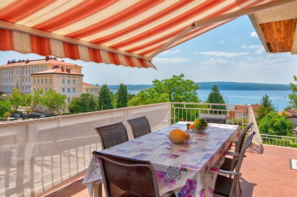 An outdoor dining area with a table set for two, overlooking a body of water and buildings.