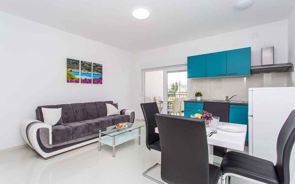 A modern living room with a grey sofa, a glass coffee table, and a dining area with a white table and black chairs.