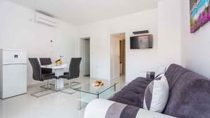 Una sala de estar moderna con una mesa de centro de vidrio, un sofá y un comedor con un refrigerador blanco y sillas negras.