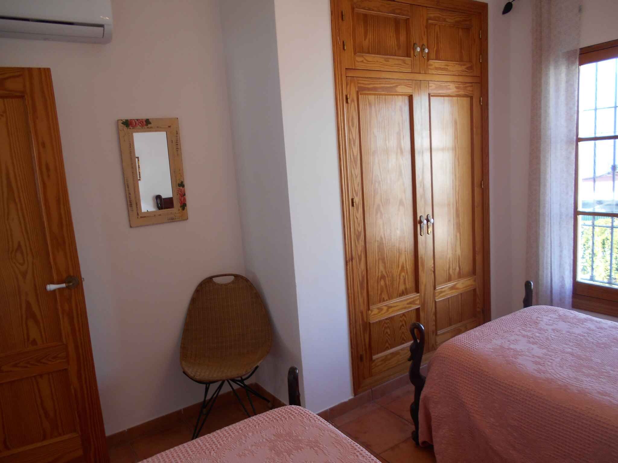 A bedroom with two beds, a wooden wardrobe, a chair, and a mirror on the wall.