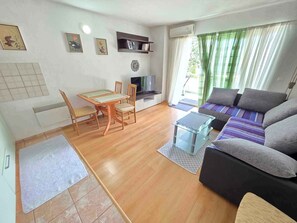 Un salon comprenant un canapé, un téléviseur, une table à manger avec des chaises et une bibliothèque.