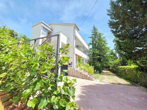 A two-story building with a balcony, a paved driveway, and surrounding greenery.