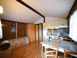 A compact room with a bed, a small table with chairs, a kitchenette, and a wooden wardrobe.