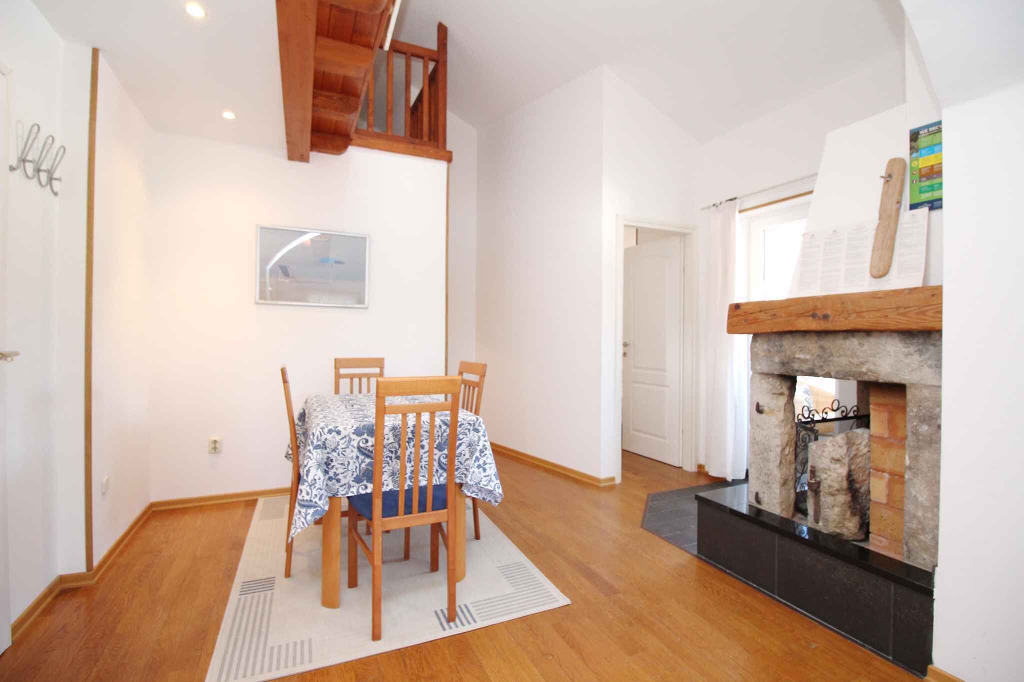 Un coin repas avec une table dressée pour quatre personnes, une cheminée et un escalier menant à l’étage supérieur.