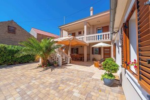 A two-story building with a balcony, outdoor seating area, and potted plants. - Holiday home Fully air-conditioned and modern (Privlaka)