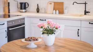 A kitchen with white cabinets, a wooden countertop, a coffee maker, a cutting board, and a vase with pink flowers. - Holiday home Fully air-conditioned and modern (Privlaka)