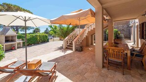 An outdoor patio with a wooden table and chairs, a barbecue grill, and umbrellas providing shade. - Holiday home Fully air-conditioned and modern (Privlaka)