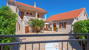 A two-story building with a red-tiled roof, a balcony, and a welcome sign. - Holiday home Fully air-conditioned and modern (Privlaka)