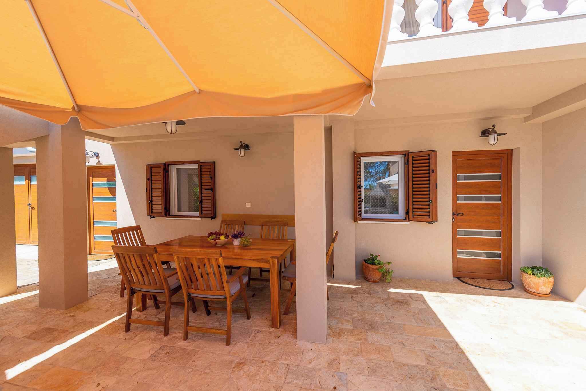 A covered outdoor dining area with a wooden table and chairs, a large umbrella, and a potted plant.