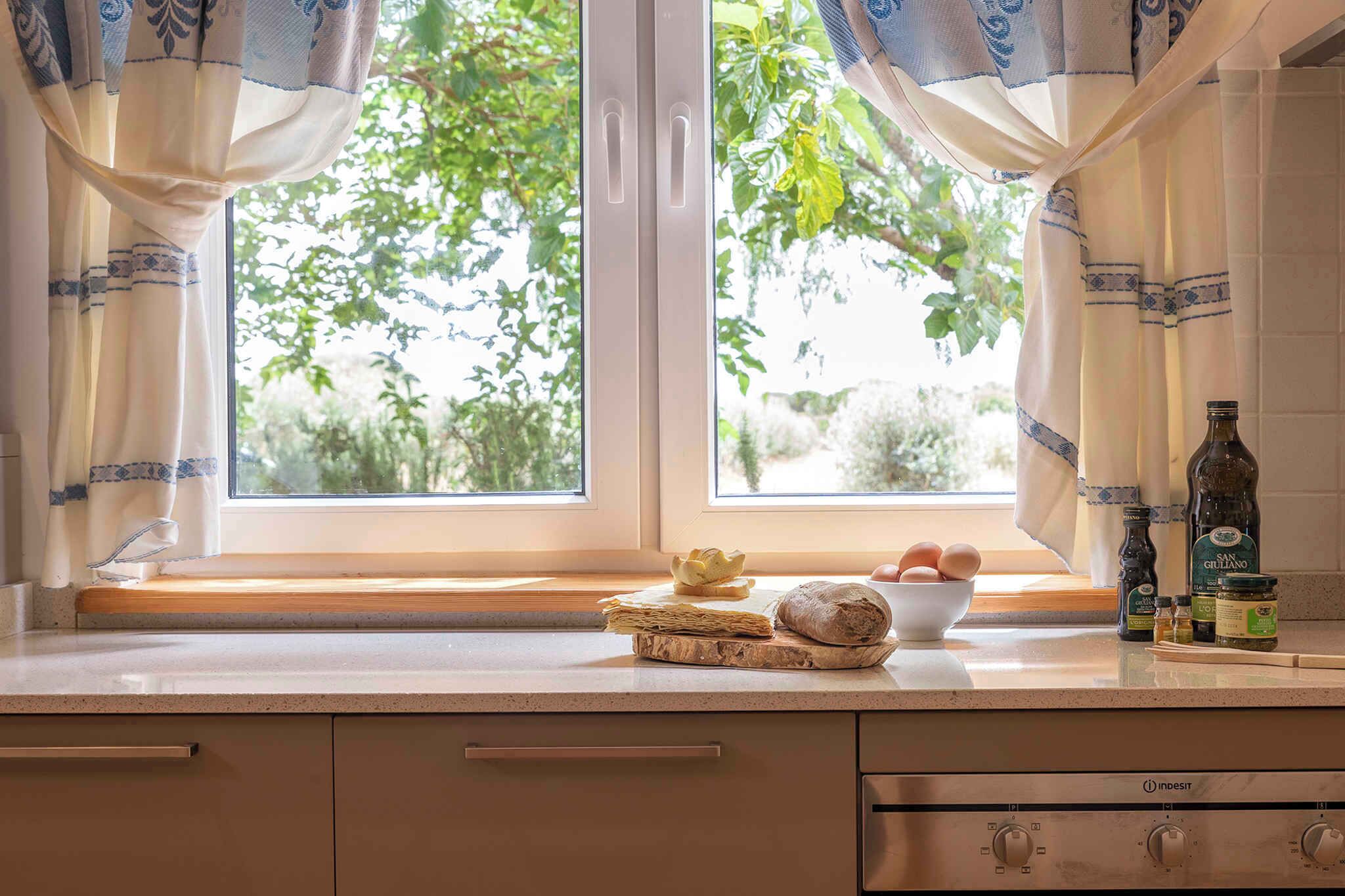 Una cocina con ventana, un bol de huevos, una hogaza de pan y condimentos en la encimera.