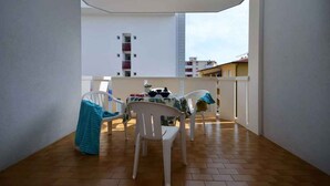 Un balcón con mesa y sillas, vista de edificios al fondo y suelo de baldosas.