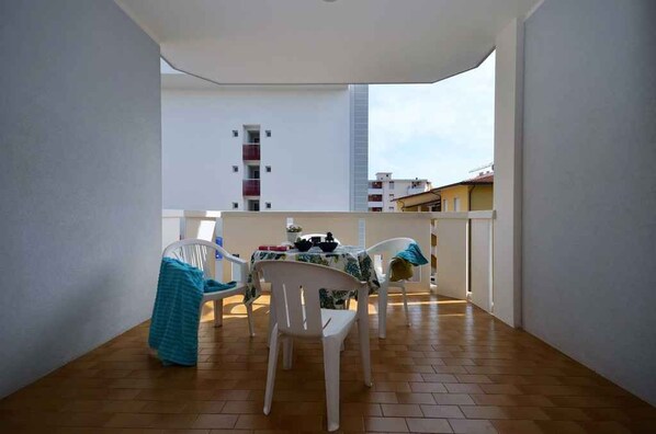 A balcony with a table and chairs, a view of buildings in the background, and a tiled floor.