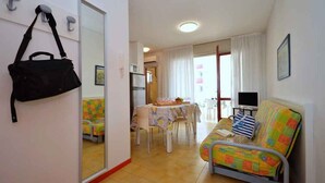 Un espacio habitable compacto con un sofá, una mesa de comedor y un televisor. Un espejo refleja parte de la habitación, y un bolso cuelga en la pared.