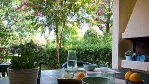 An outdoor dining area with a table set for two, surrounded by lush greenery and flowering trees. - Holiday apartment with air conditioning and terrace (Bibione)