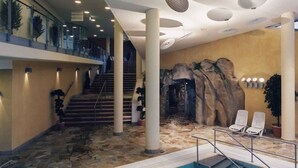 A modern indoor swimming pool with a stone floor, a staircase, and a rock wall mural. - Holiday apartment at the Therme Obernsees (Mistelgau-Obernsees)