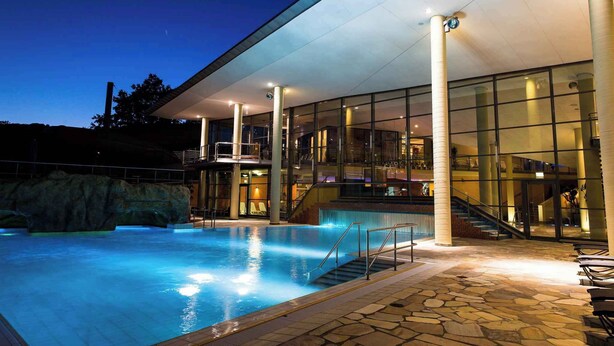 A modern building with a swimming pool, large glass windows, and a stone-tiled deck. - Holiday apartment at the Therme Obernsees (Mistelgau-Obernsees)