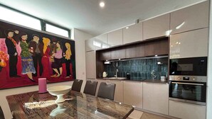 Uma cozinha moderna com área de jantar, destacando uma pintura grande, uma mesa de mármore e eletrodomésticos embutidos.