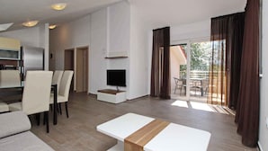 Un salon moderne avec un canapé, une table à manger, un téléviseur et un balcon agrémenté de rideaux.