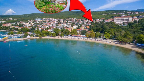 A coastal town with a beach, boats, and a large building with a red roof.